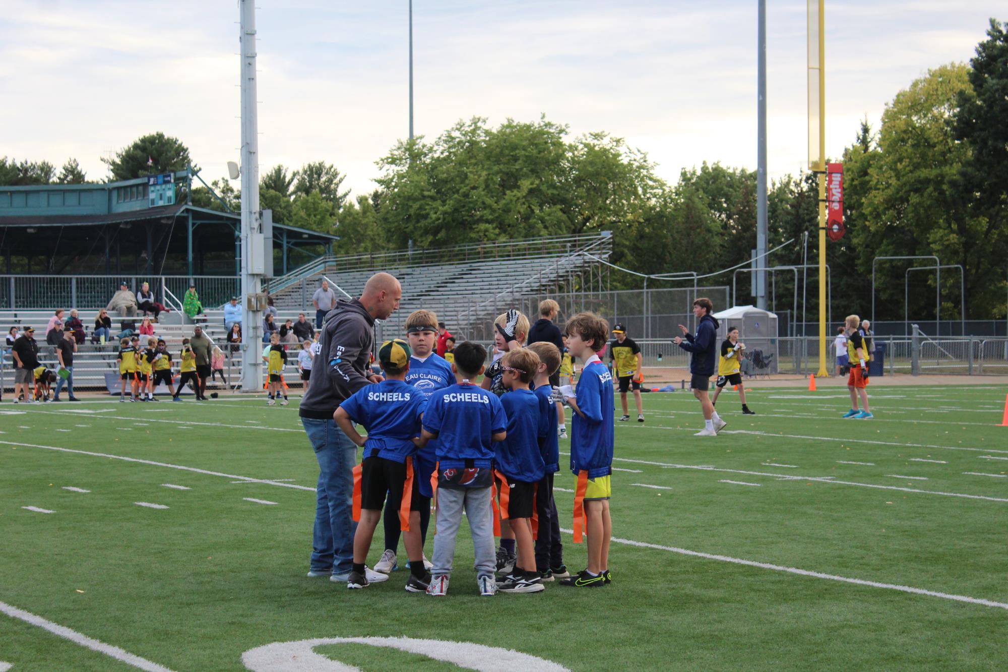 Youth Flag Football Team huddled with their coach on Carson Park's Football field.