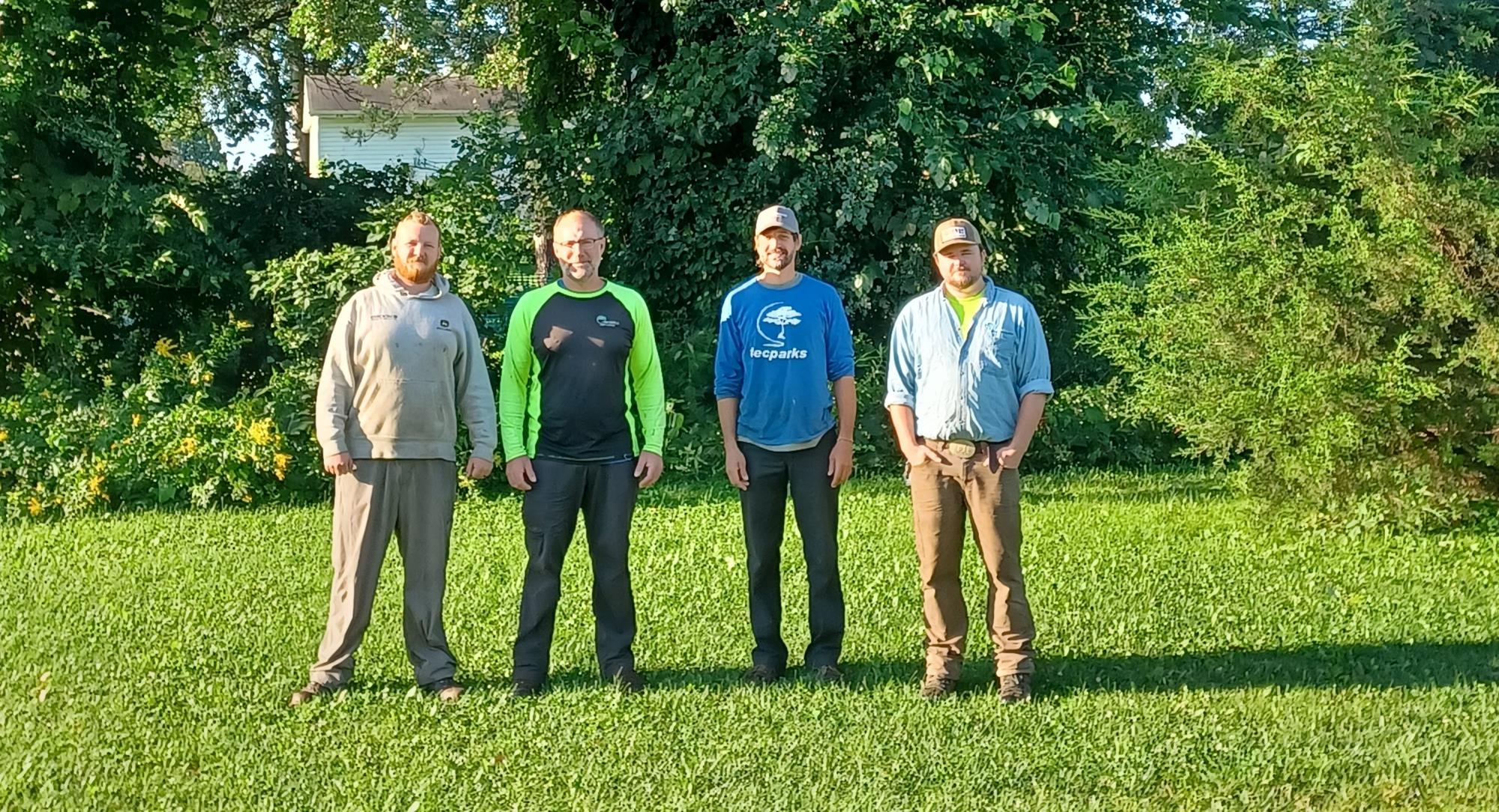 A photo of the Forestry crew, four men, standing in front of a large tree