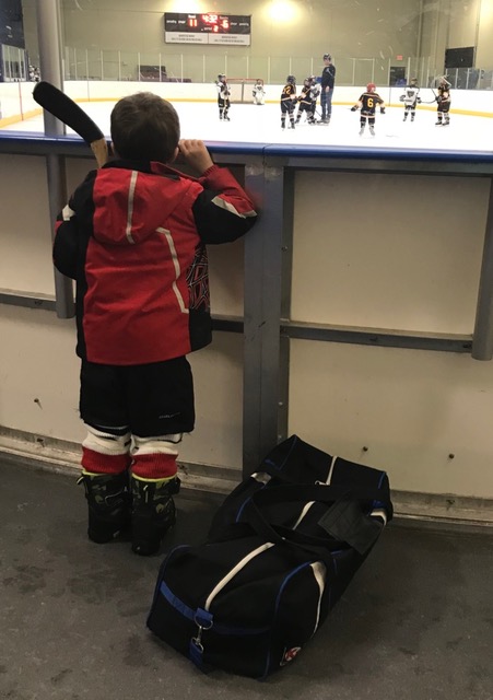 photo of a young boy peering over the rink to watch players skate